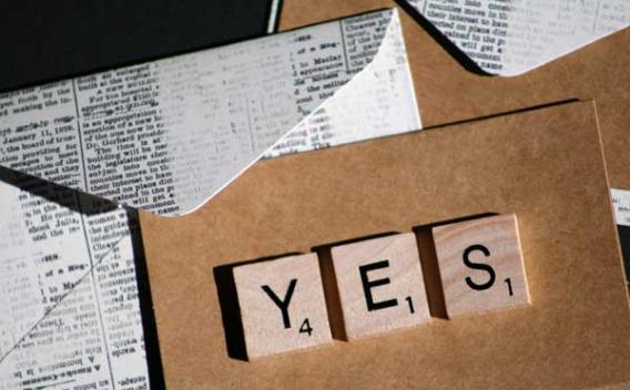 The word "Yes" spelled out on wood blocks with envelops and paper in background