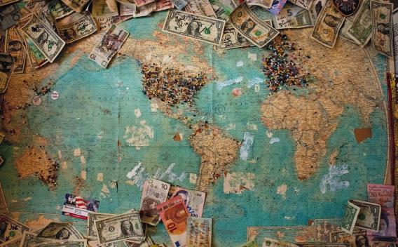 World map with dollar bills and other currencies scattered around the edges